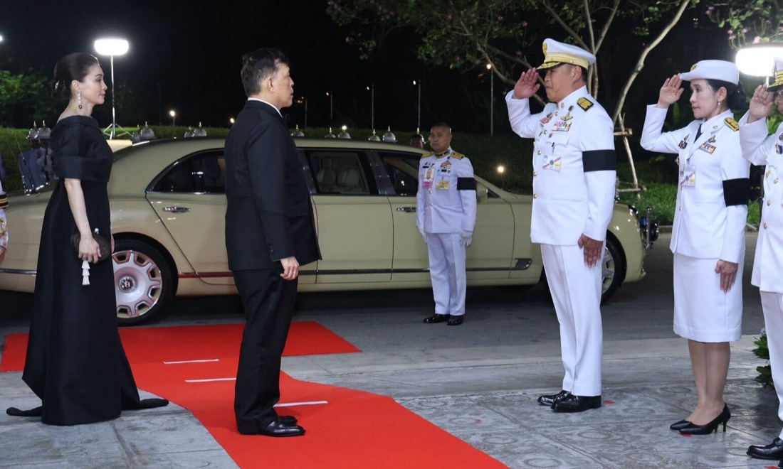 His Majesty the King and Her Majesty the Queen arriving on the red carpet at Mahidol Siddhachada Hall, received by naval officers in full ceremonial salute.