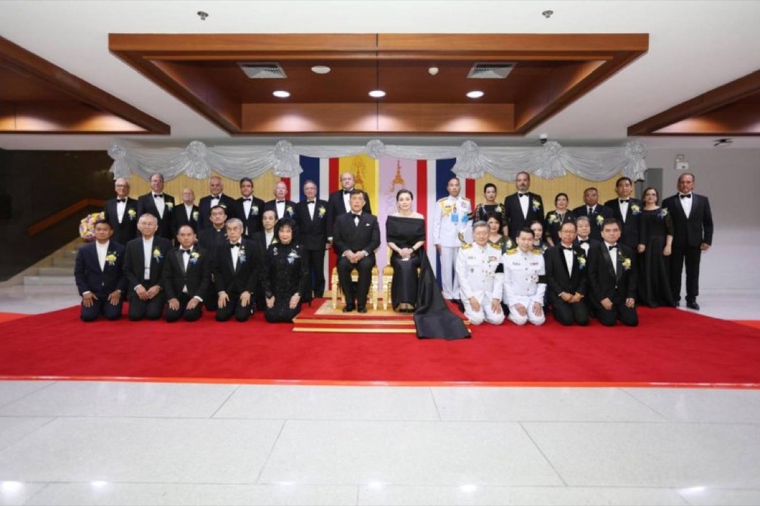 A formal portrait of dignitaries, sponsors and orchestra leadership gathered before the Thai national flag, marking the conclusion of the National Unity Concert.